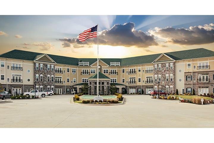 A large, multi-story building with an American flag in front under a dramatic sunset sky.