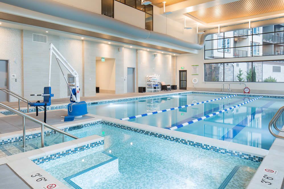 A modern indoor swimming pool with designated lanes and a pool lift, featuring large windows and bright lighting.