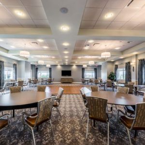 A modern conference room with round tables and chairs, featuring a large screen and carpeted flooring.