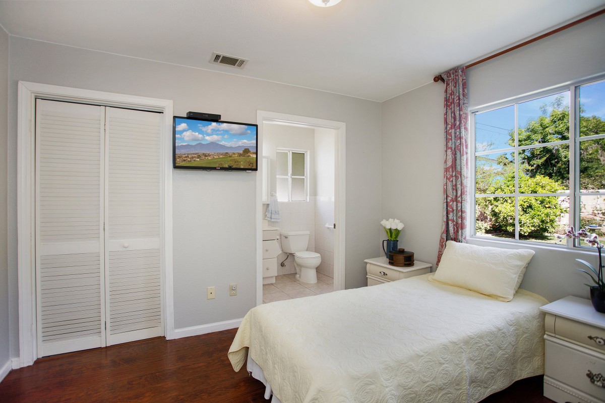 A minimalist bedroom with modern decor, featuring a comfortable bed, wall-mounted television, and large window for natural light.
