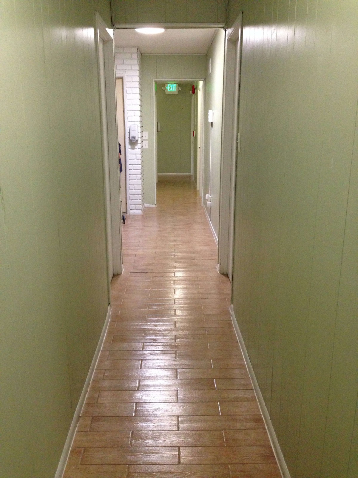 A long hallway with green walls and tiled flooring, lined with doors on either side.
