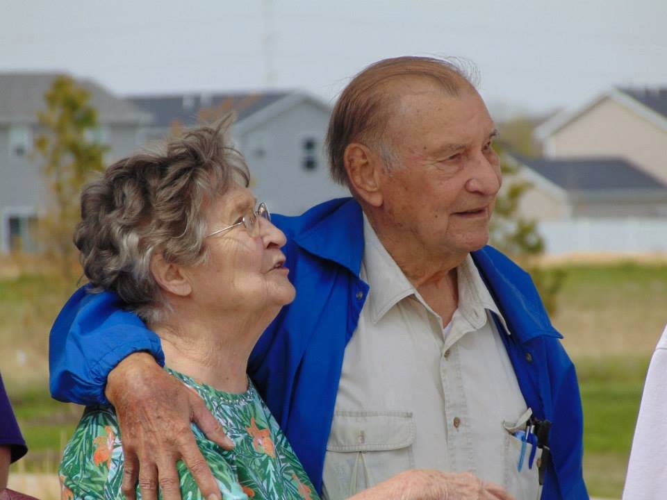 An elderly couple enjoying a moment outdoors, embracing each other warmly.