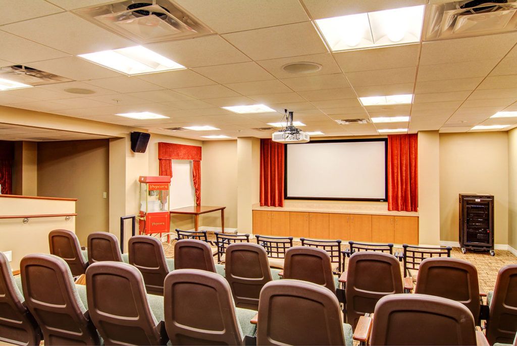 An empty indoor theater with rows of seating facing a large projection screen.