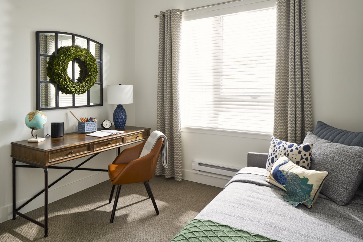 A cozy home office with a wooden desk, brown chair, and large window letting in natural light.