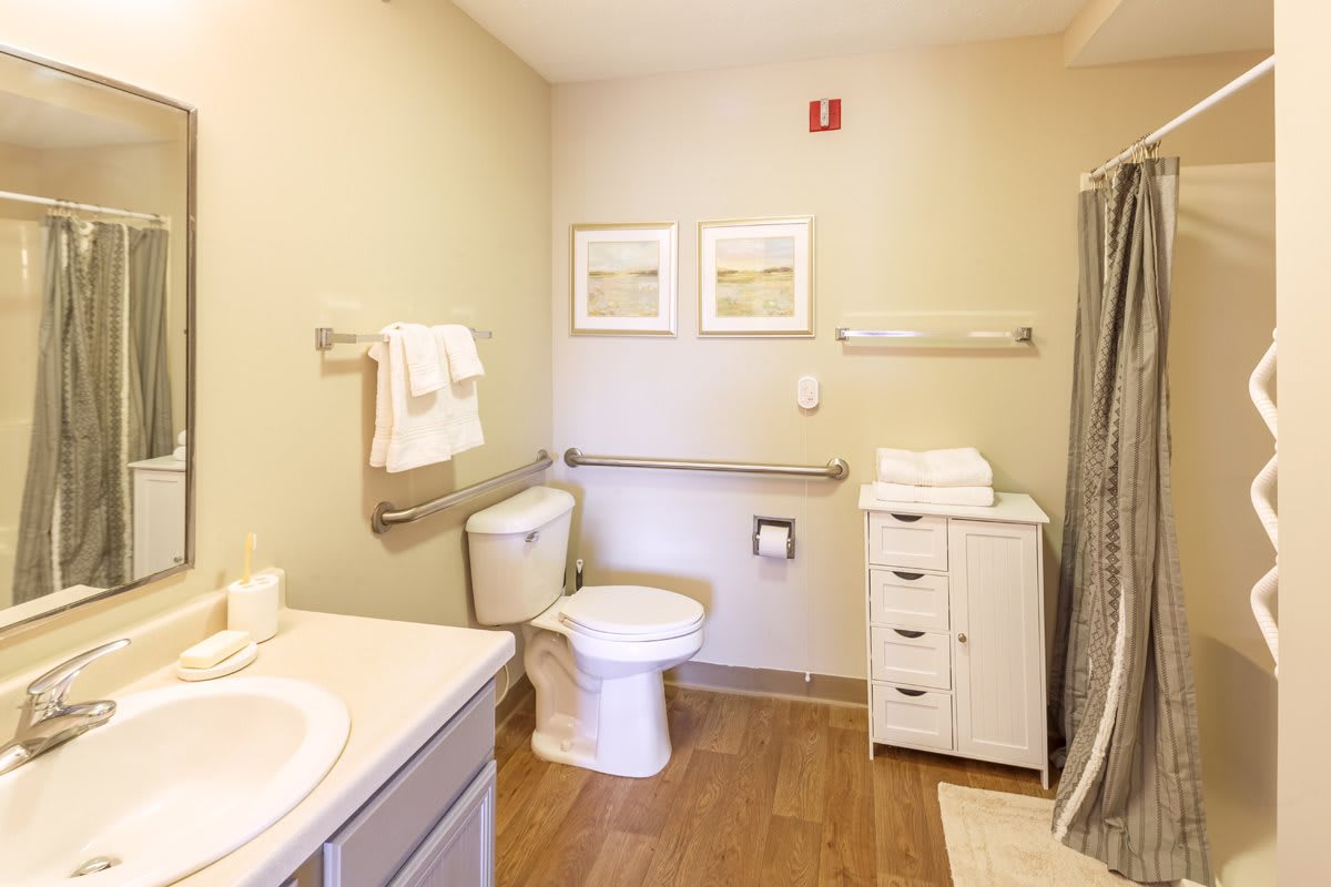 A clean and organized bathroom featuring a toilet, shower, sink, and storage cabinet with neatly arranged towels.