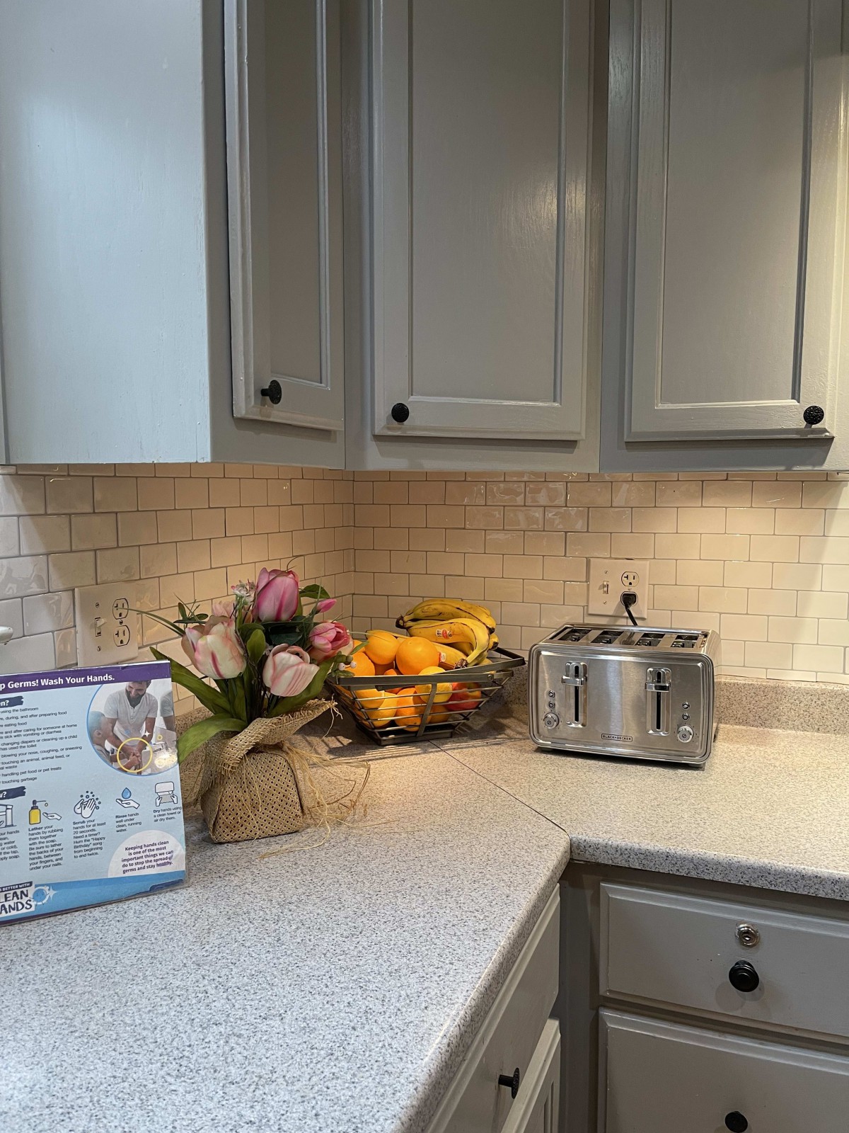 A cozy kitchen corner featuring a toaster, a fruit bowl, and fresh flowers on the counter.
