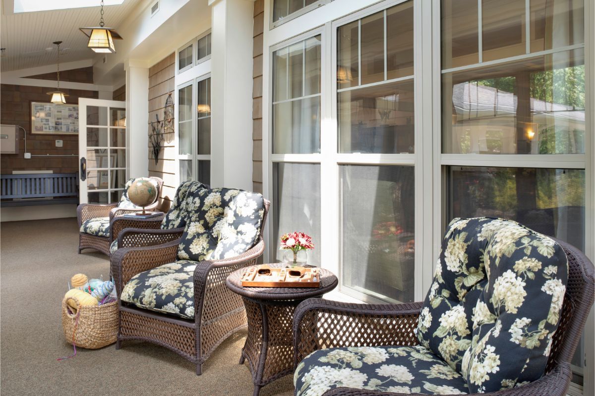 A cozy patio area with wicker chairs and floral-patterned cushions arranged next to a small table by large windows.