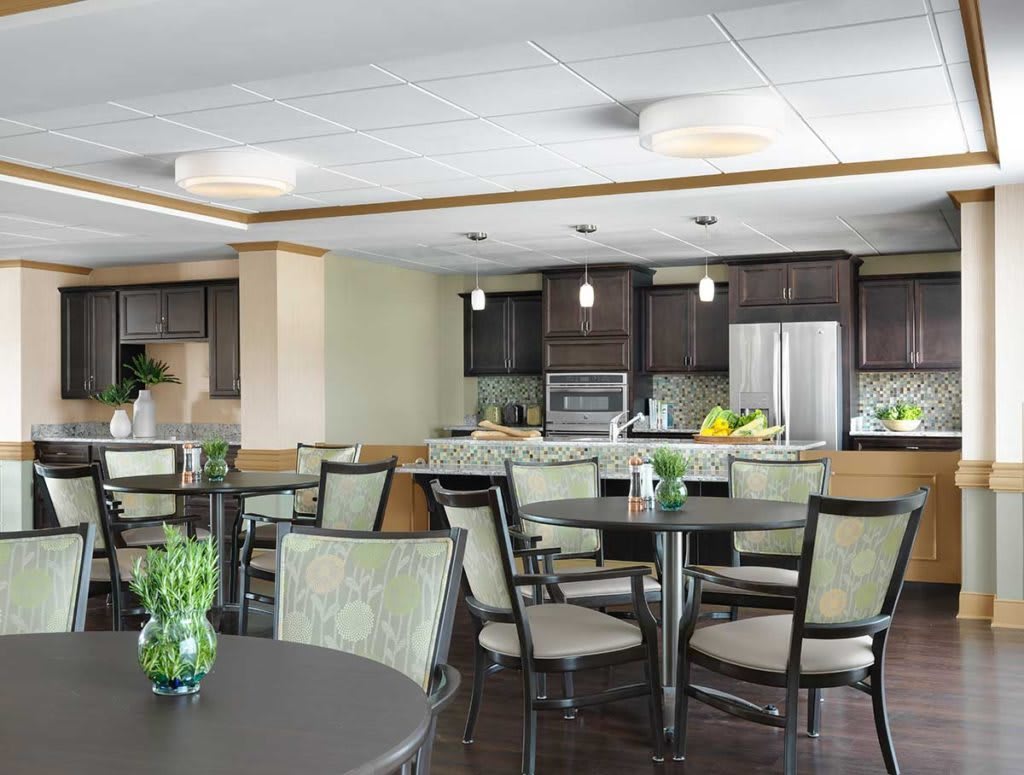 A modern dining area with tables and chairs adjacent to a kitchen, featuring sleek appliances and contemporary lighting.