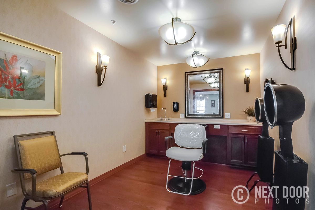 An empty salon room featuring a chair, mirror, and warm lighting.