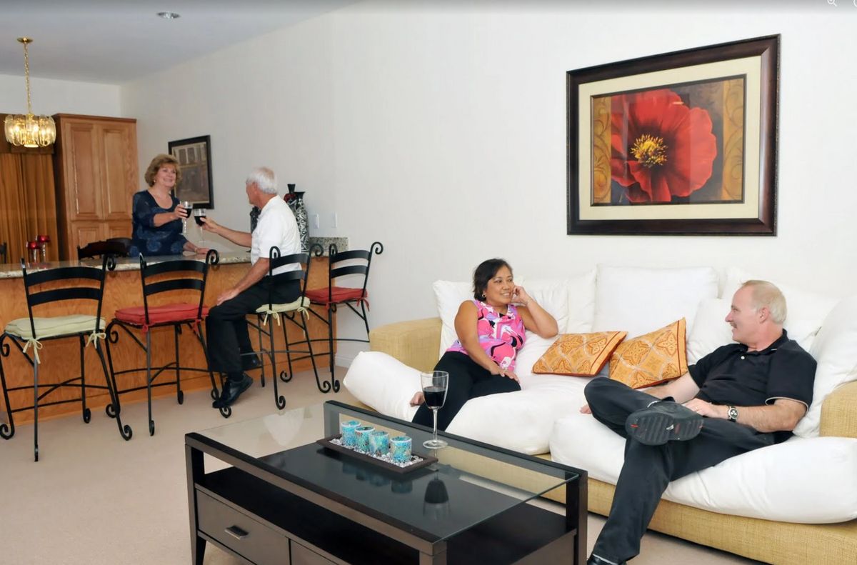 A group of people relaxing and conversing in a stylish living room with a bar area.