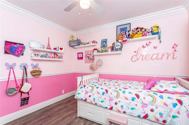 A brightly decorated child's bedroom with a pink color scheme, featuring a bed with colorful bedding, wall art, and organized shelves displaying toys and decor.