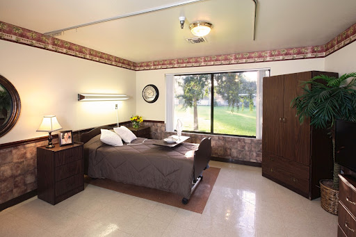 A cozy and well-lit bedroom with a simple design, featuring a bed, nightstand, and large window offering a view of the outdoors.