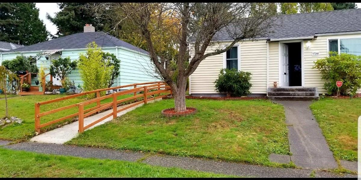 A cozy neighborhood house with a tree in the front yard and a wooden accessibility ramp leading to the entrance.