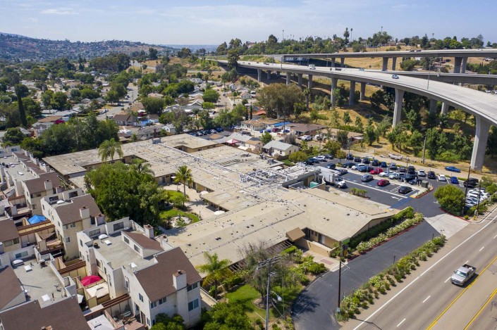 Aerial view of a suburban area with buildings, parking lots, and a nearby highway.