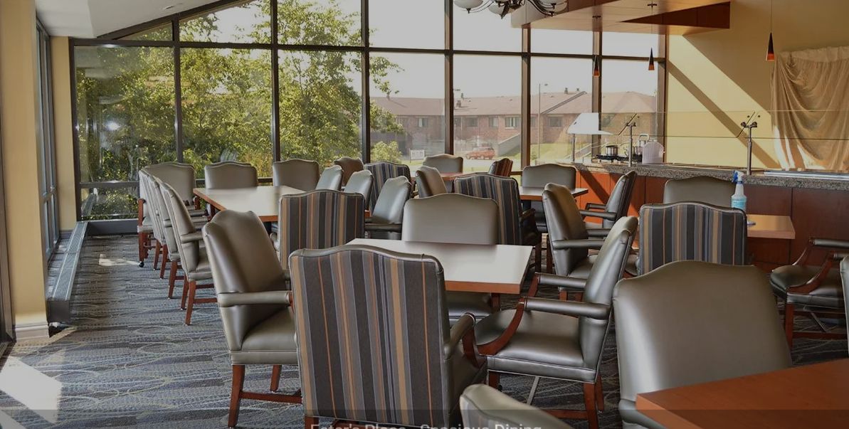 A dining area with multiple chairs and tables near large windows.
