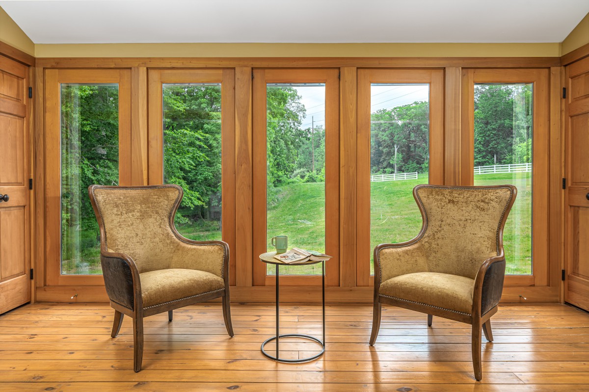 A cozy interior space with two elegant chairs facing large windows, offering a serene view of nature outside.