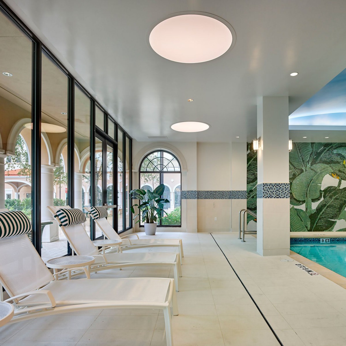 A modern indoor pool area with lounge chairs and large windows.