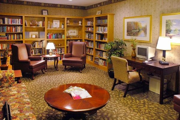 A cozy library reading area with bookshelves, armchairs, and a computer desk.