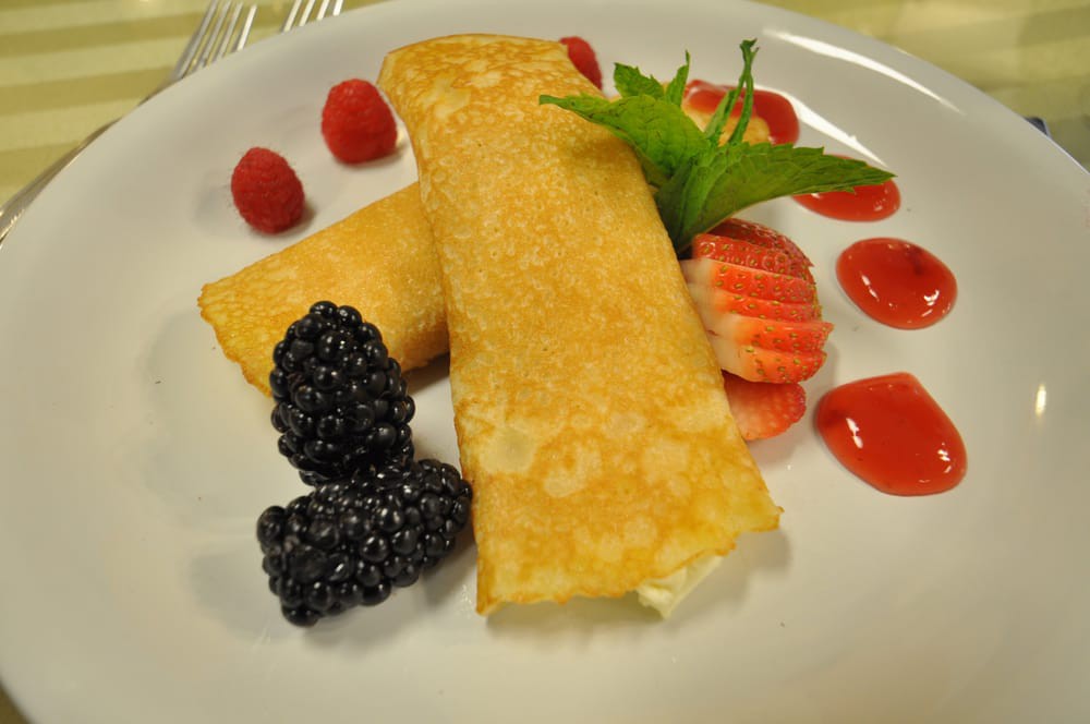 A beautifully plated dessert featuring crepes with fresh berries and a garnish.