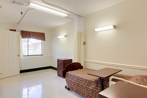 An empty hospital patient room featuring a bed, a window with curtains, and minimal furniture.