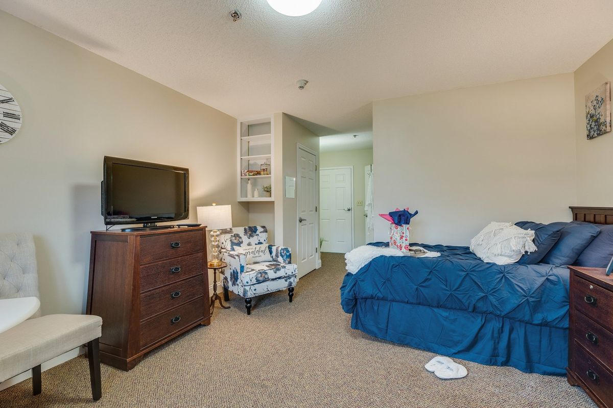 A cozy bedroom featuring a bed with blue bedding, a TV on a dresser, and a comfortable chair.