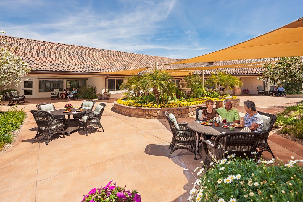 A sunny courtyard with people sitting at patio tables surrounded by lush greenery.
