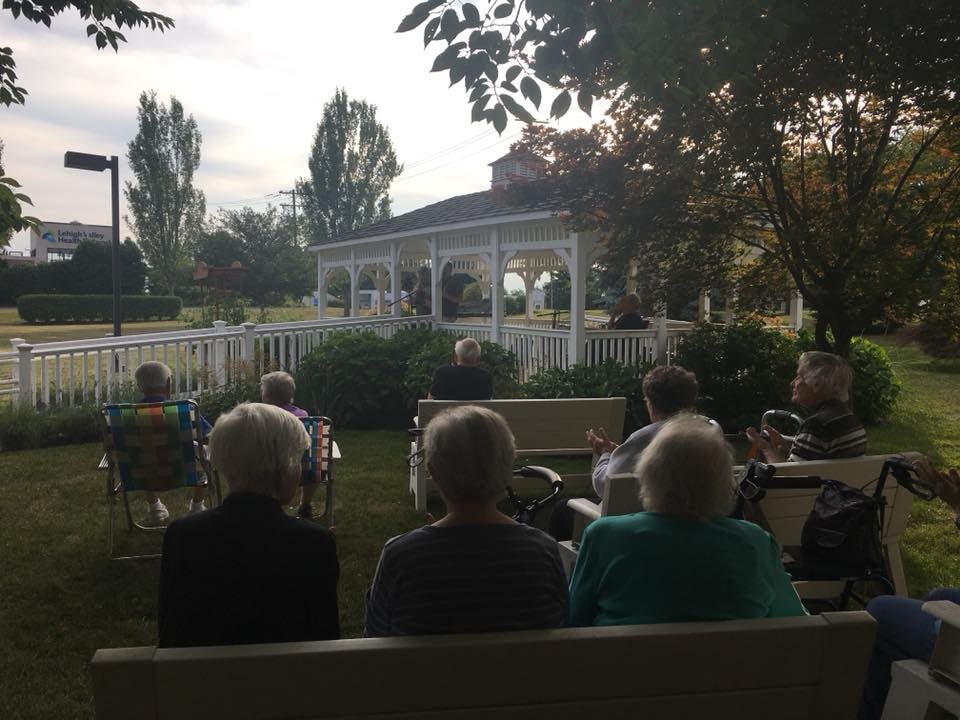 A group of seniors sitting outdoors, facing a gazebo during a social event.