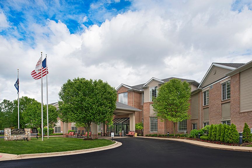 A brick building with a driveway and flagpole under a cloudy sky.
