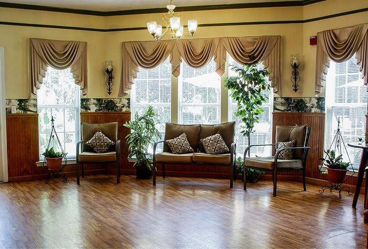 A cozy living room with elegant decor, featuring a sofa, chairs, and large windows adorned with curtains.