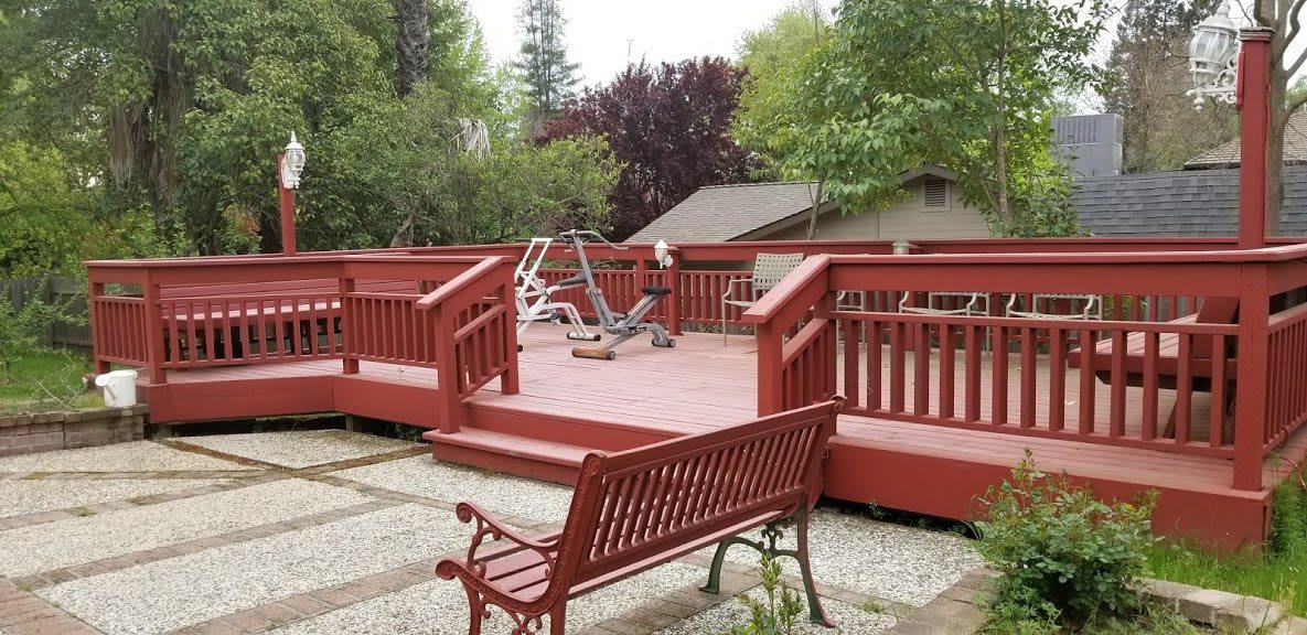An outdoor deck with exercise equipment and a bench, surrounded by trees.