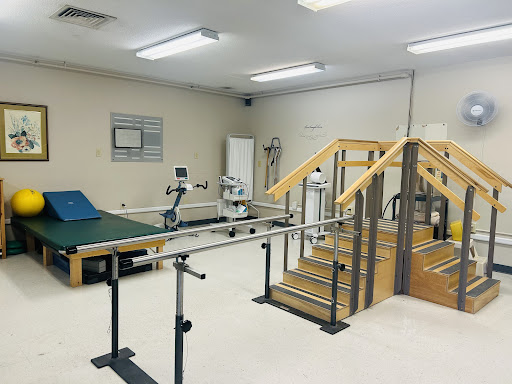 A physical therapy room equipped with parallel bars, stairs, and various exercise equipment.