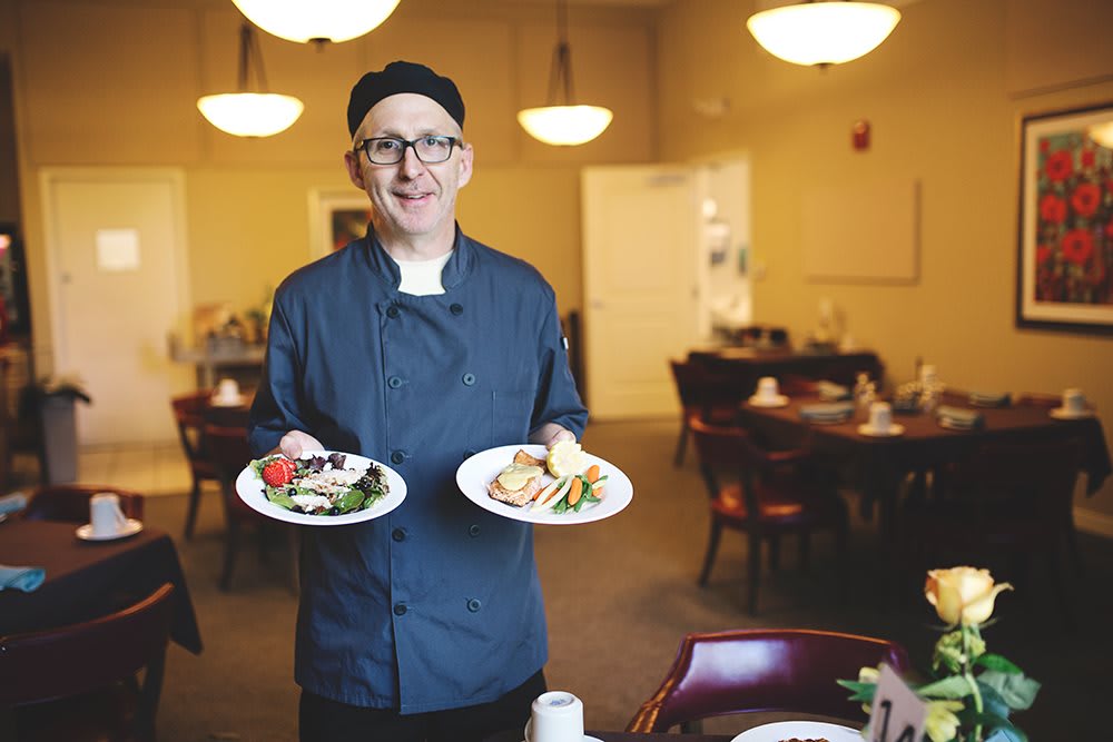 A chef presenting two plates of food in a restaurant setting.