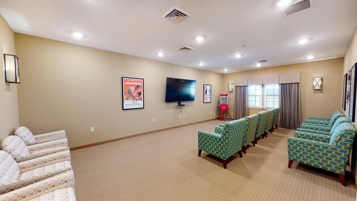 A small theater room with a large screen TV, comfortable seating, and wall posters.
