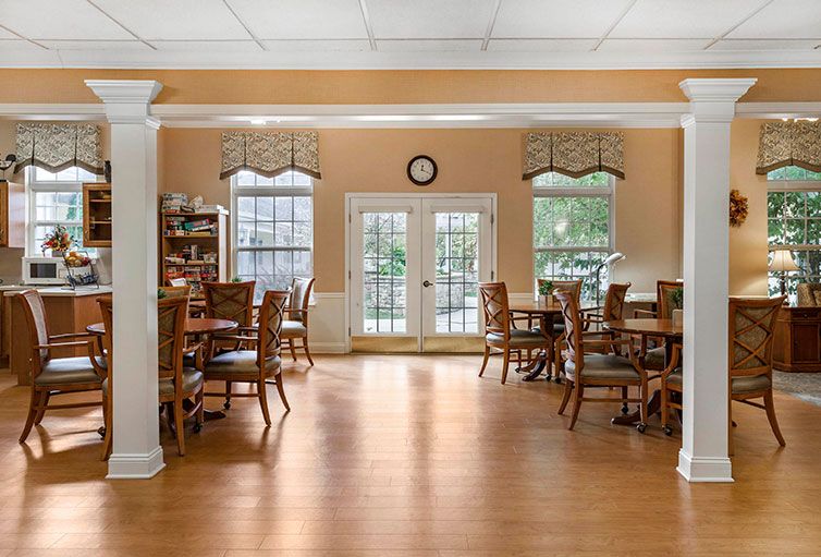 A spacious dining room with several wooden tables and chairs, featuring large windows that let in natural light.