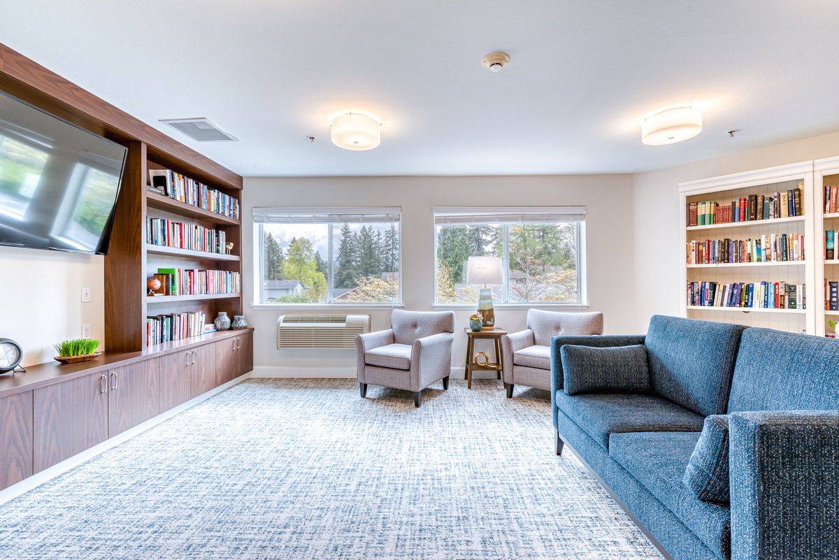 A cozy living room with a large bookshelf, comfortable seating, and natural light from the windows.