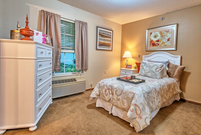 A cozy bedroom with a single bed, dresser, and soft lighting.
