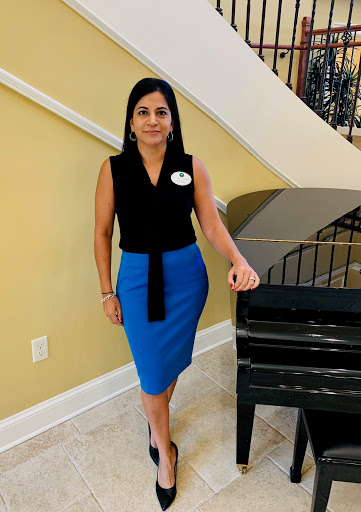 A woman in a stylish black top and blue skirt poses elegantly beside a piano.
