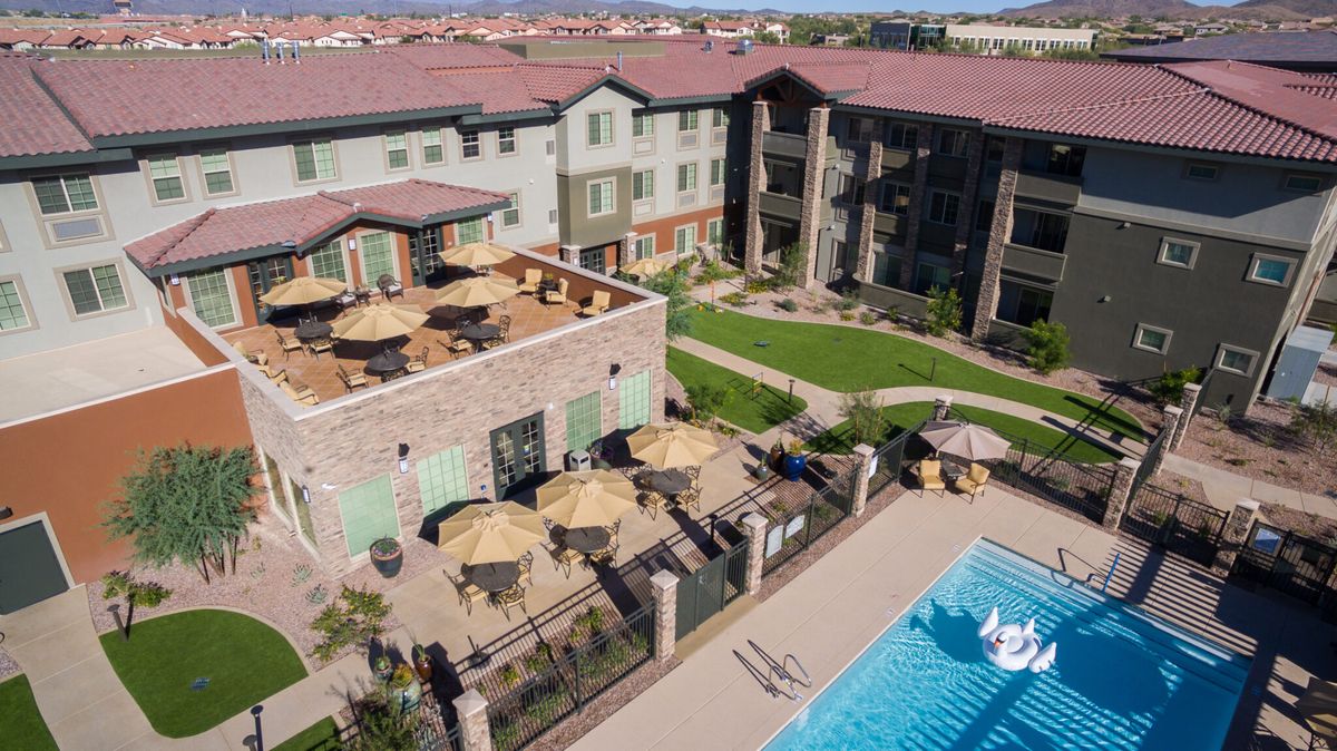 A modern apartment complex featuring a well-maintained outdoor pool, patio with umbrellas, and landscaped lawns.