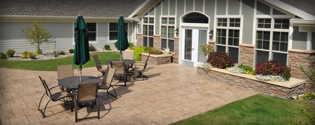 A cozy patio area with outdoor furniture and an umbrella, adjacent to a house with well-maintained landscaping.