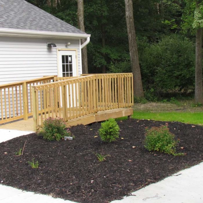 A wooden ramp leading to a house with landscaped mulch and plants.