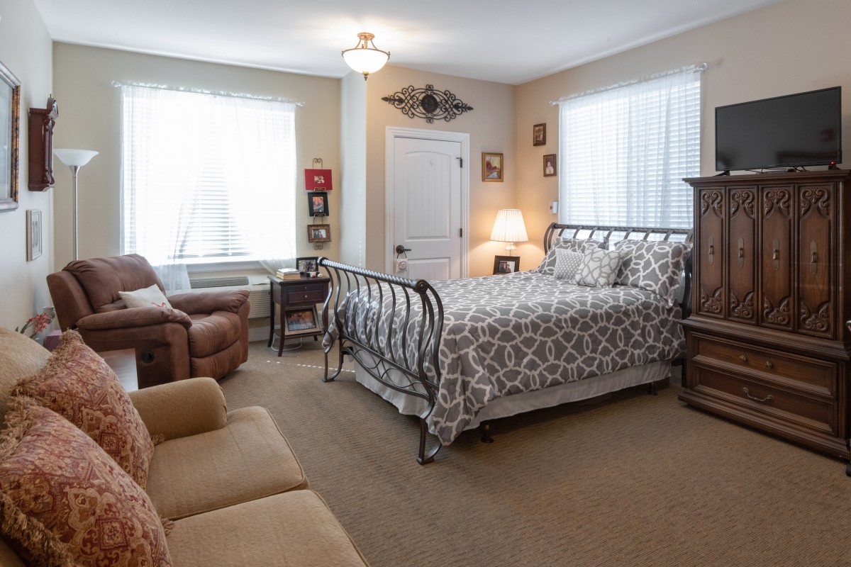 A cozy bedroom featuring a metal-framed bed, sofa, armchair, and decorative elements.