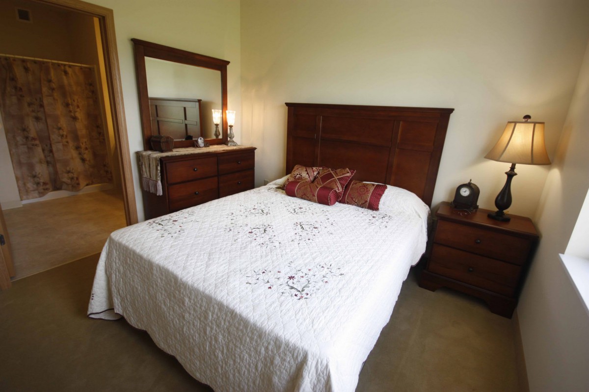 A cozy bedroom with a neatly made bed, wooden dresser, and mirror.