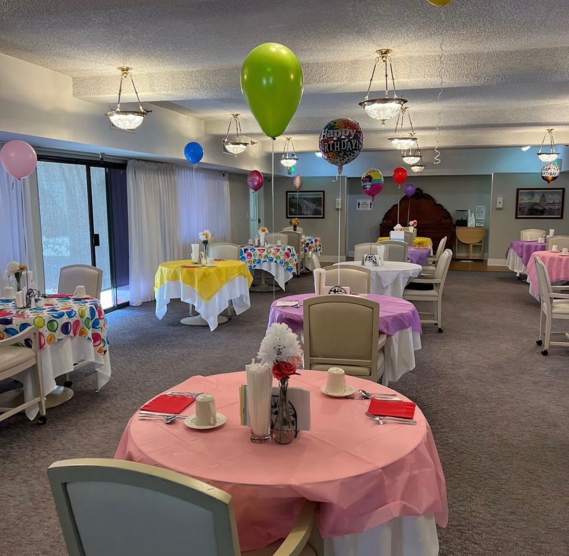 A festive dining area with decorated tables and colorful balloons set for a celebration.