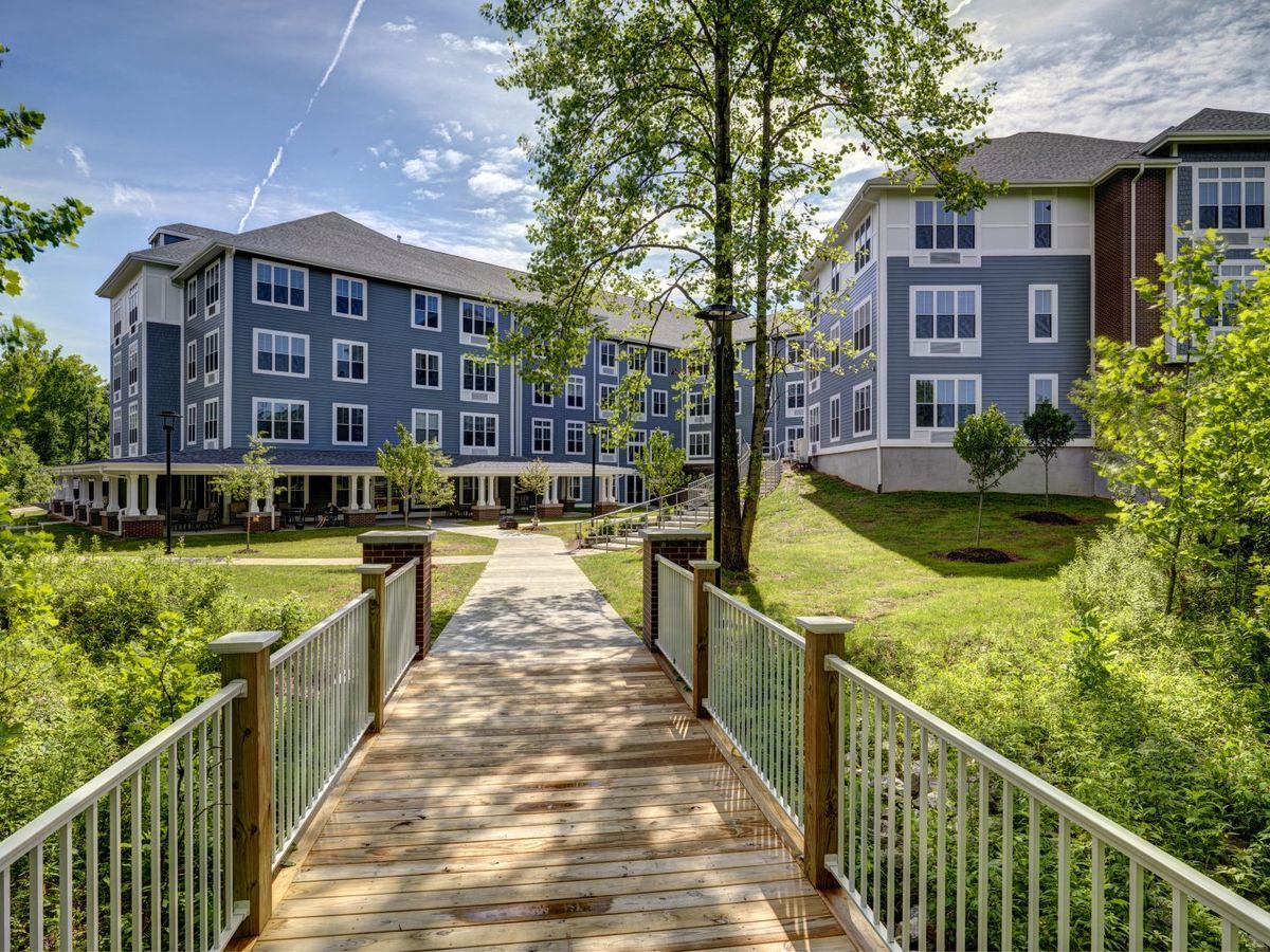 A picturesque scene of a modern apartment complex with a wooden bridge and lush greenery.