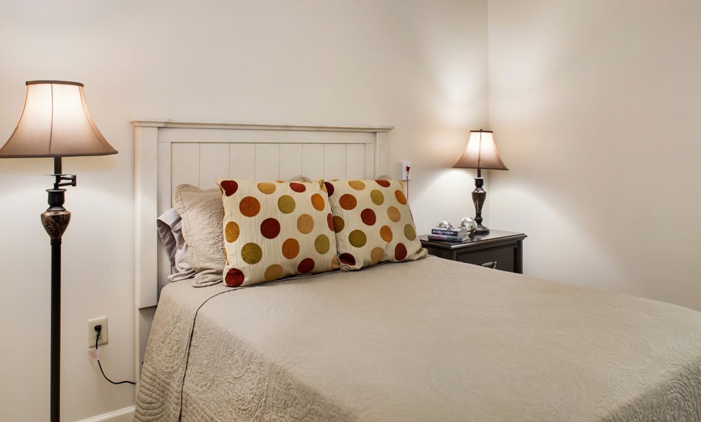 A cozy bedroom with a neatly made bed, colorful polka dot pillows, and a bedside lamp on a nightstand.