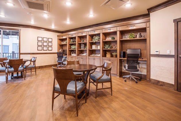 A well-lit library or office space with wooden bookshelves, a round table, and chairs.