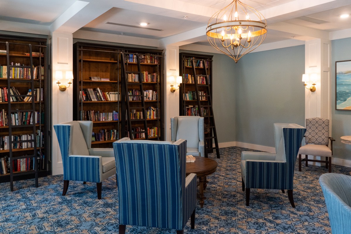 A cozy library room with bookshelves, armchairs, and a chandelier.