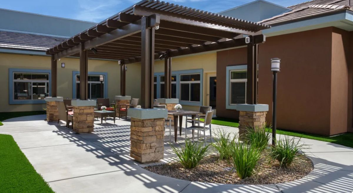 A modern patio with a pergola and outdoor seating area, surrounded by landscaping.