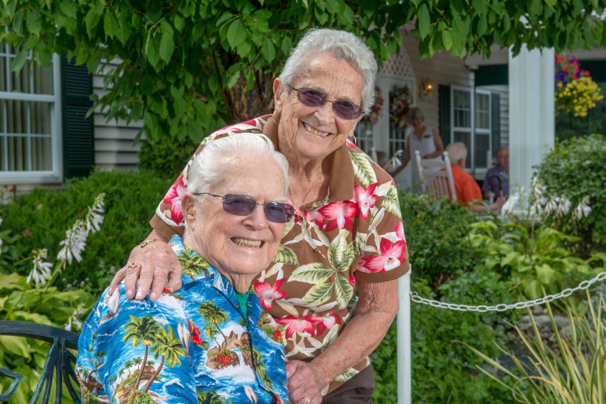 A cheerful senior couple wearing colorful shirts and glasses, smiling outdoors.