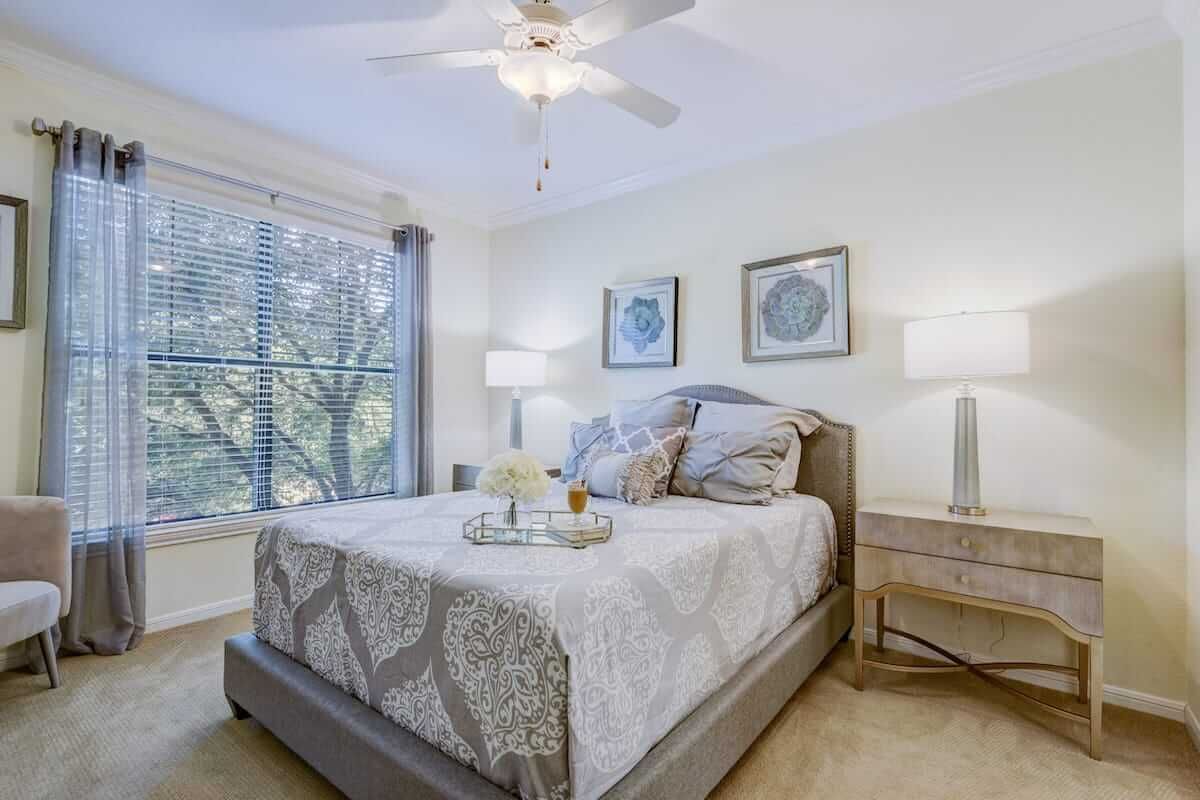 A modern bedroom with a well-decorated bed, large window letting in natural light, and soothing neutral tones.
